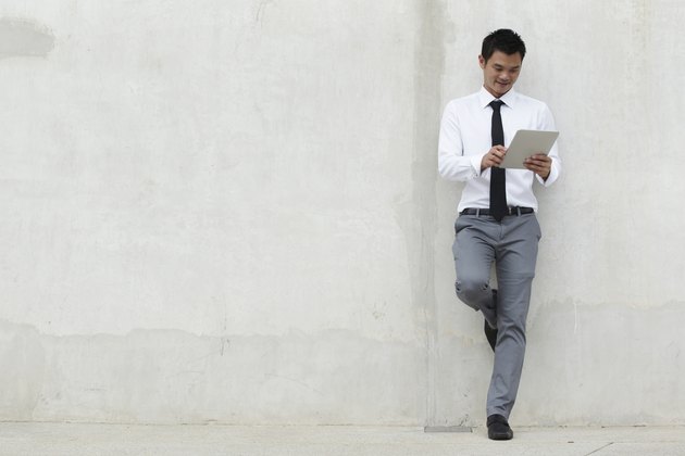 Young businessman reading while leaning on a blank wall