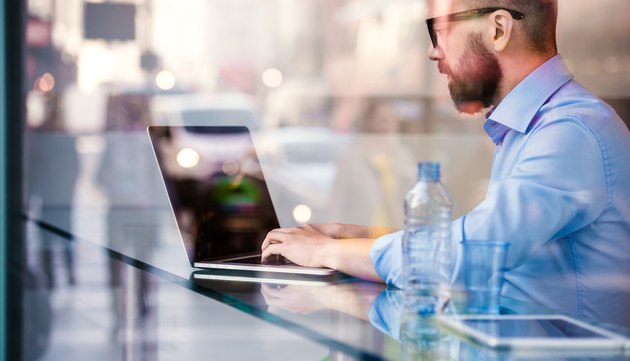 Hipster manager in cafe, working on laptop by window