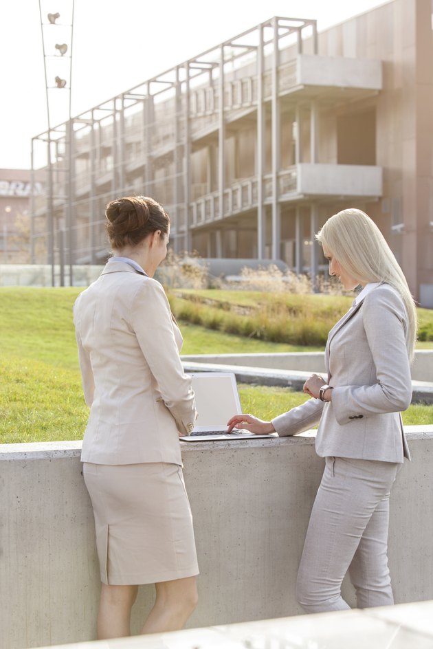 Young businesswomen working together on laptop while standing against office building