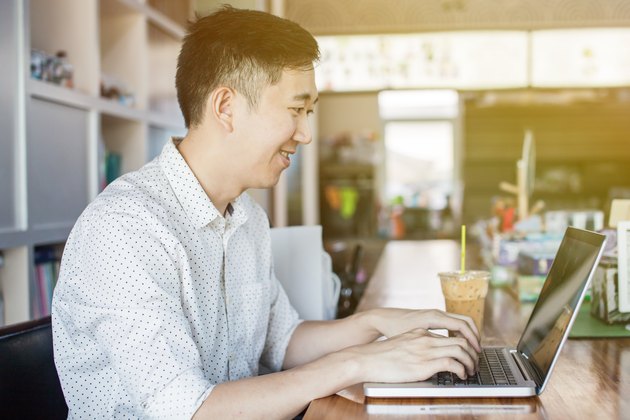 Handsome Asian man with computer in cafe (focus on face)