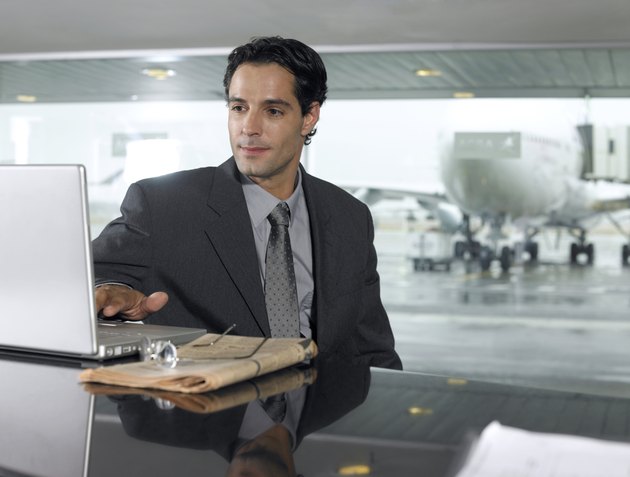 Businessman using laptop computer in airport, close-up