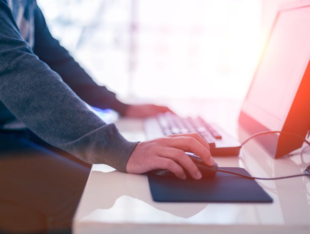 Male hand holding computer mouse with laptop keyboard