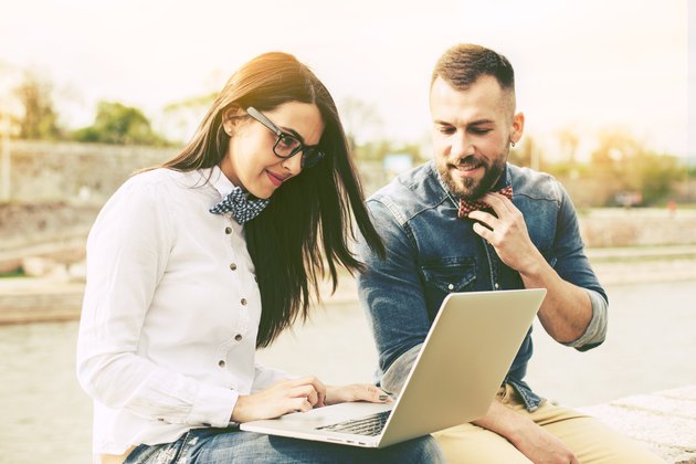 Couple of hipster friends using laptop in the city