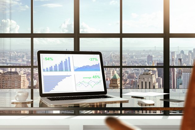 Financial statistics on laptop screen on glassy table in modern