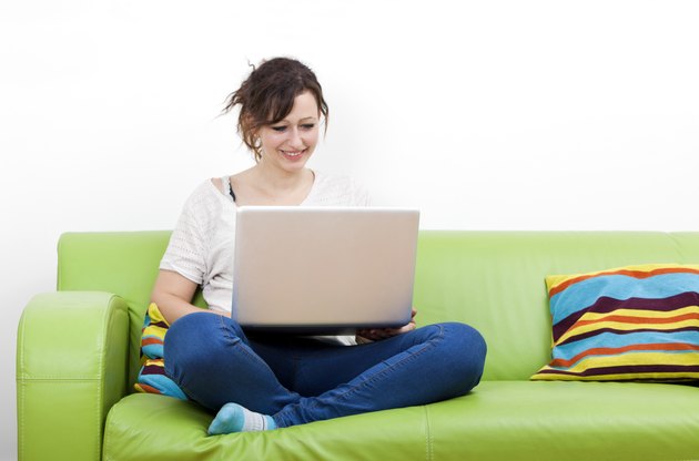 Full length of happy young woman using laptop while sitting on green sofa