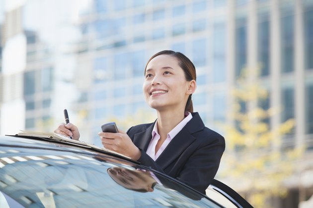 Businesswoman Standing by Car Using Phone and Taking Notes
