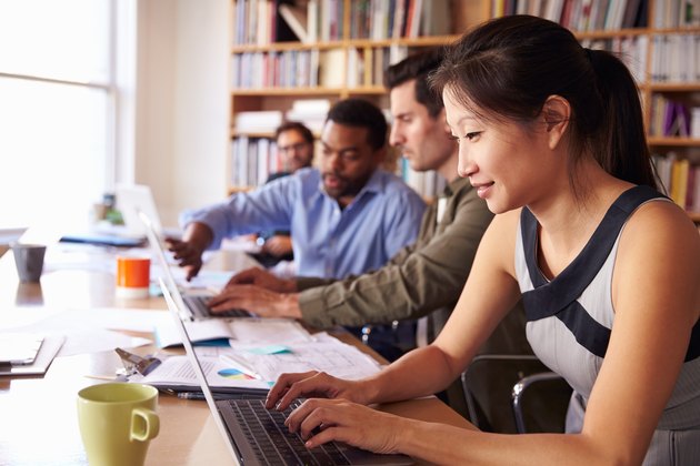 Businesswoman Using Laptop At Desk In Busy Office