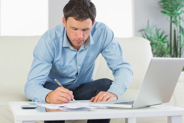 Serious casual man writing on sheets paying bills