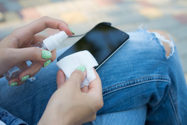 Female hand holding spray and cloth for cleaning the phone