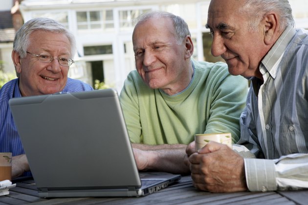 Three senior men looking at laptop computer screen, smiling, close-up