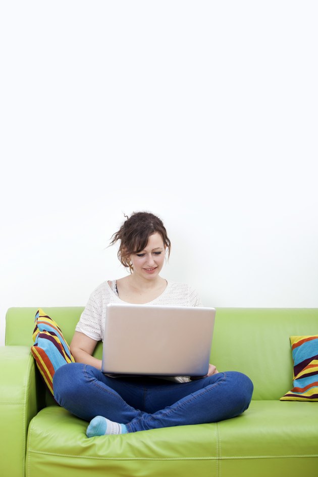 Full length of happy young woman using laptop while sitting on green sofa