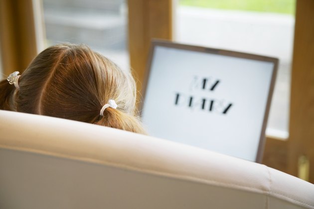 Girl (5-7) sitting on sofa with laptop, rear view