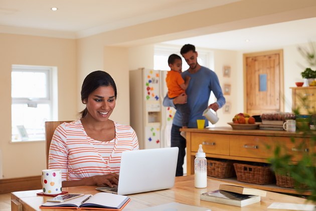 Family In Kitchen With Mother Using Laptop At Table