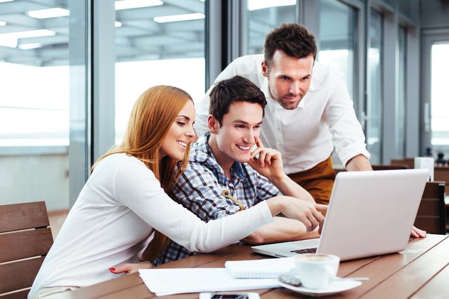 Smiling students sitting in a canteen with a laptop
