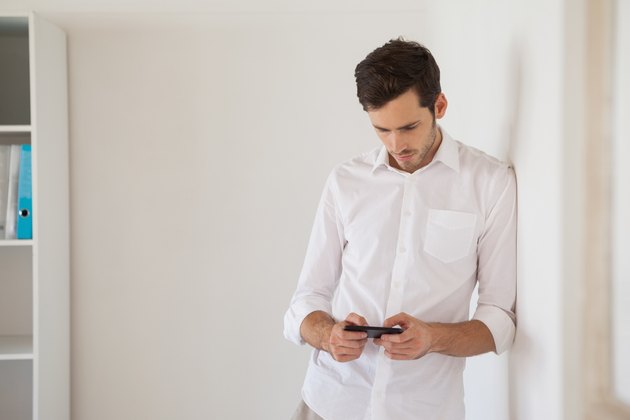 Casual businessman leaning against wall sending a text