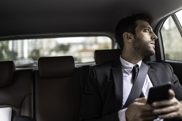 Businessman using cellphone in a cab and looking through window