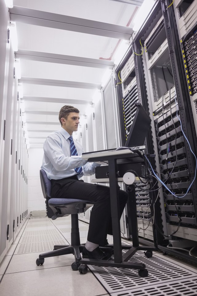 Technician sitting on swivel chair using laptop to diagnose servers