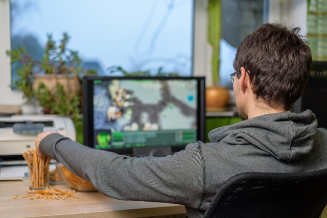 male gamer playing strategy game on computer eating snacks