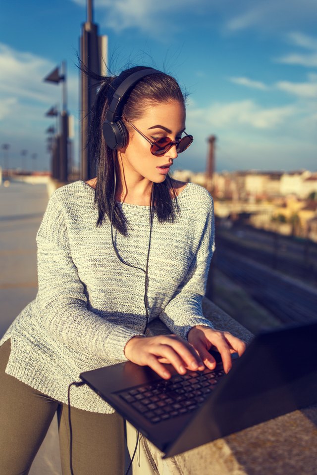 Young hipster woman typing on laptop outdoor