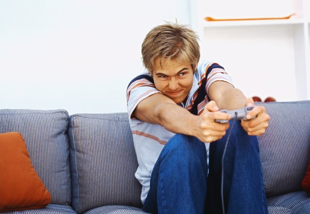 Front view of young man sitting on sofa and playing computer game