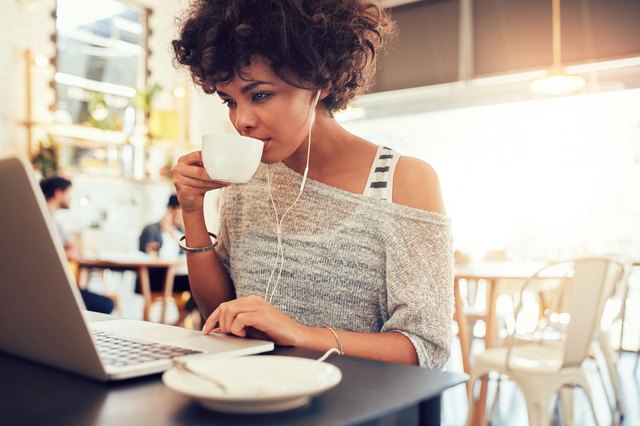 Young african woman drinking coffee and using laptop at cafe