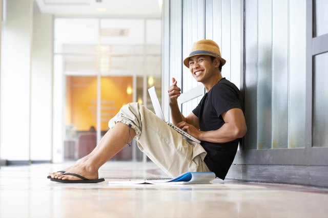 Portrait of a college student sitting in a corridor with a laptop on his lap