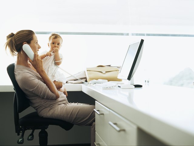 side profile of a businesswoman sitting in front of a computer and talking on a telephone with her daughter sitting beside her